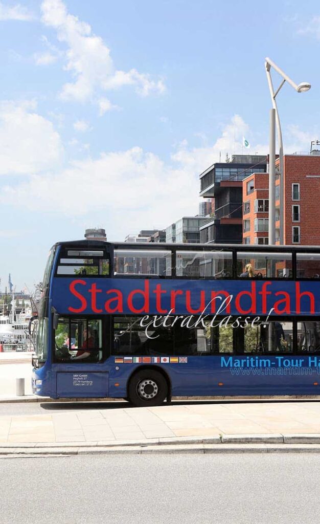 Blauer Cabrio-Doppeldeckbus der Stadtrundfahrt Hamburg vor historischer Kulisse.